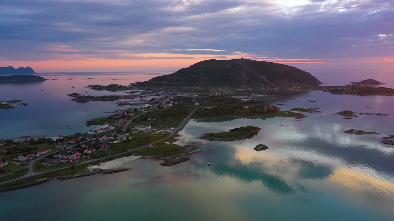 Aerial view overlooking the village on Sommaroy island and Hillesoy mountain, reflecting Arctic sea, during, midnight sun, tranquil, sunny, summer evening, in Troms, Norway - tracking, drone shot