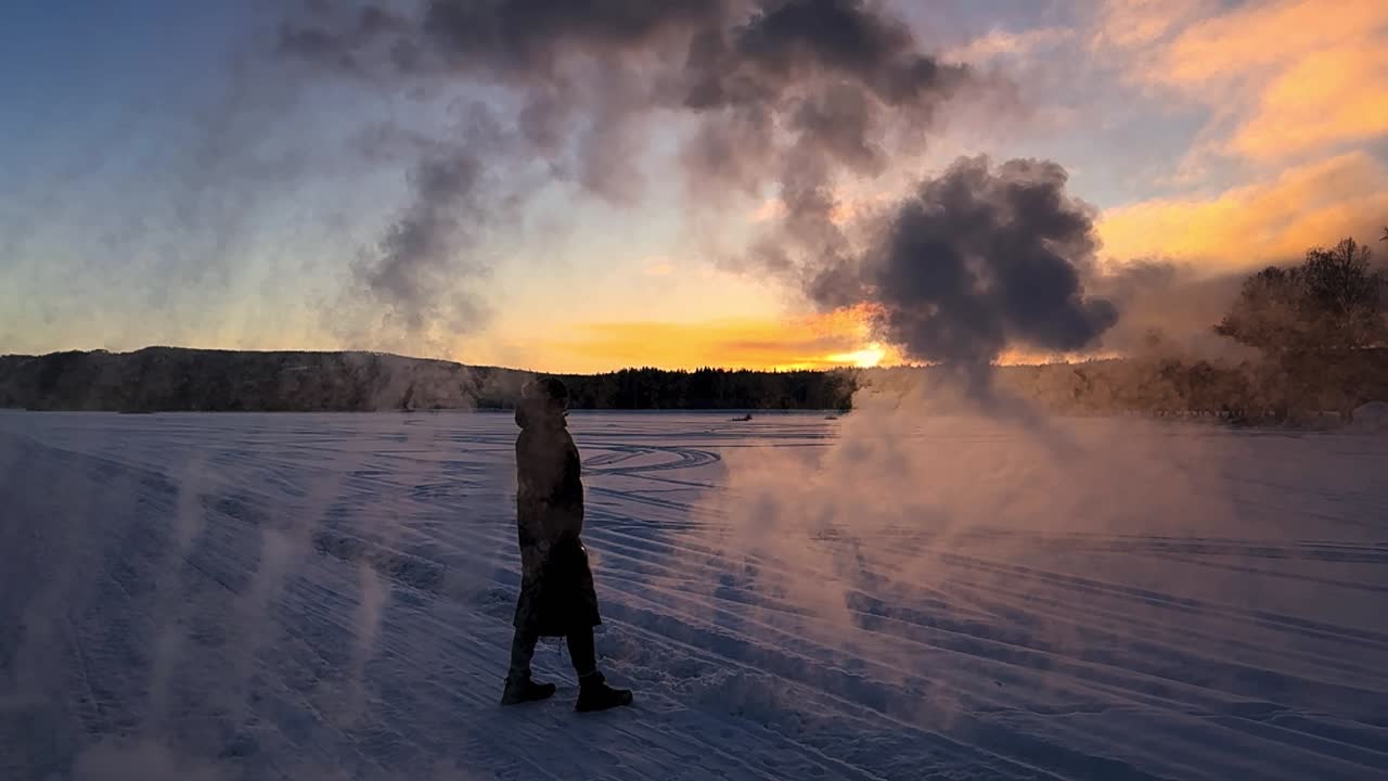 A woman throwing a can of water creating a mist of snow on a cold evening i Sweden. A Silhouette during sunset. Static shot in slow motion