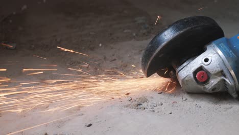 sierra circular de metal cortando una parte metálica en el piso de hormigón generación de chispas naranjas. trabajador corta metal con chispas anaranjadas volando. movimiento lento
