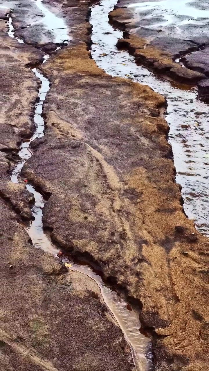 Piccolo ruscello che serpeggia attraverso un paesaggio arido, crepato e secco in vista aerea verticale