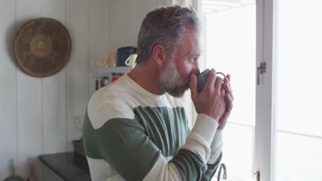 Kaukasischer-Reifer-Mann,-Der-Durch-Das-Fenster-Schaut-Und-Kaffee-Trinkt