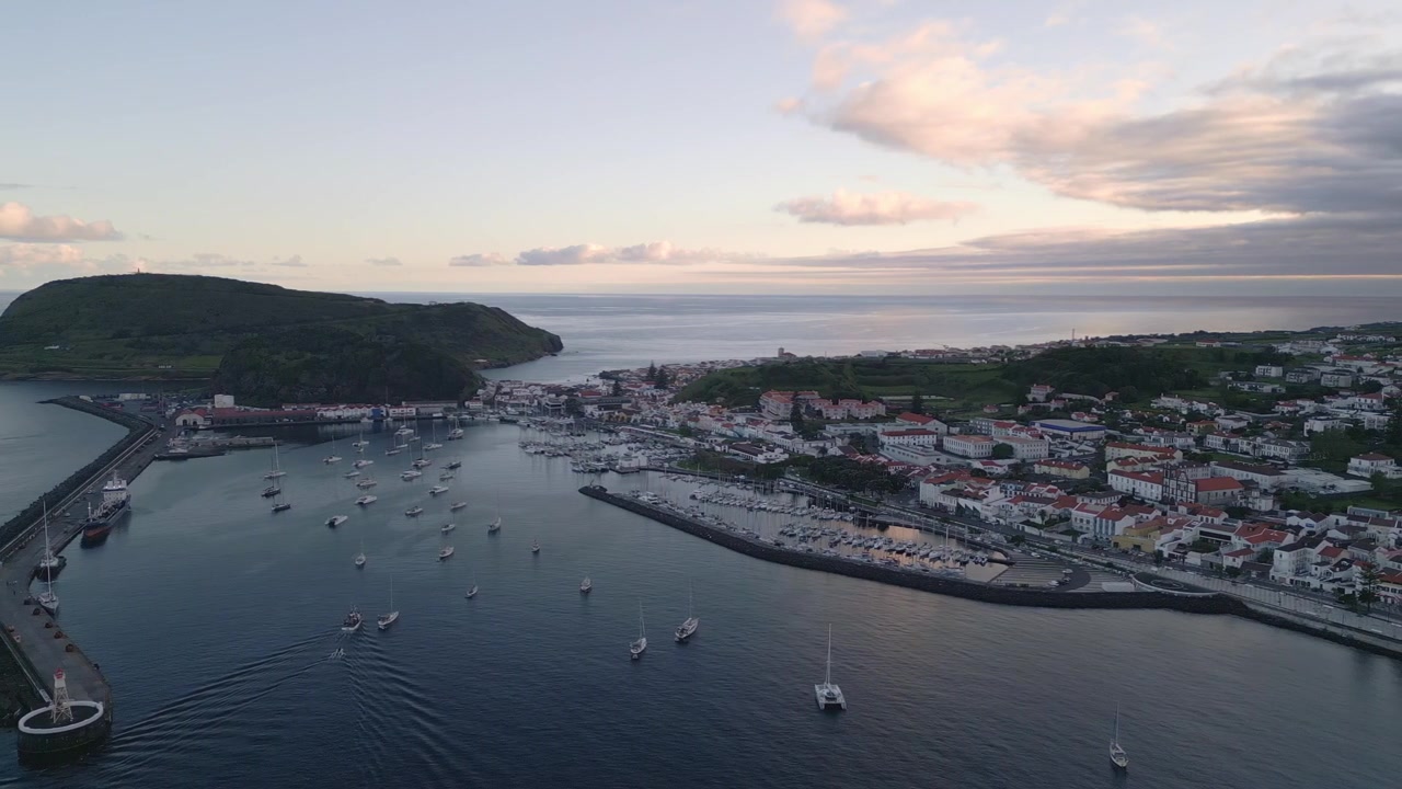 Marina di Horta al tramonto sull'isola di Faial, Azzorre, Portogallo, che mostra il porto, il lungomare, le barche ormeggiate e la calda luce serale sull'Oceano Atlantico, ripresa aerea.