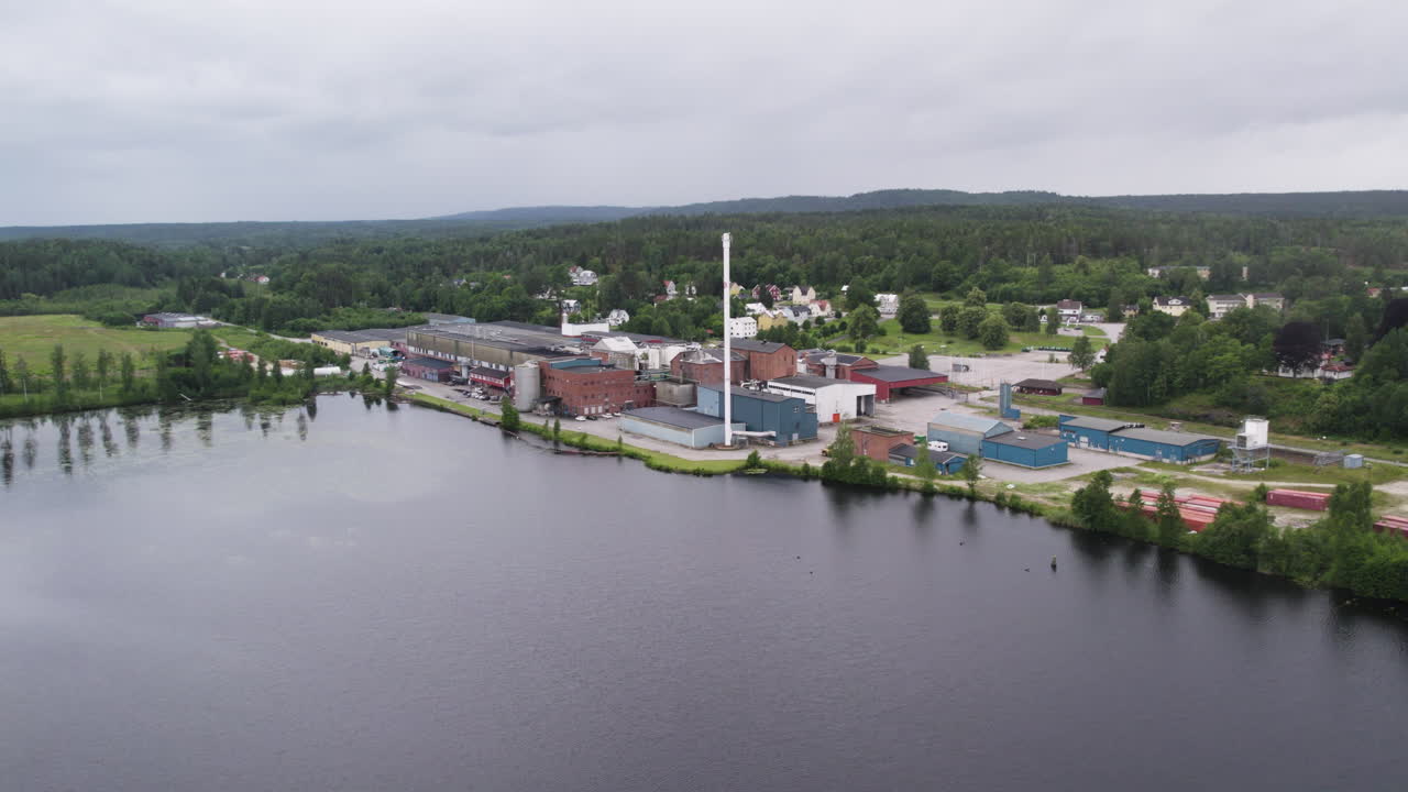 Establishing drone shot of Hafrestroms Foretagspark during the day with body of water and trees, industry in Asensbruk, Dalsland, Sweden