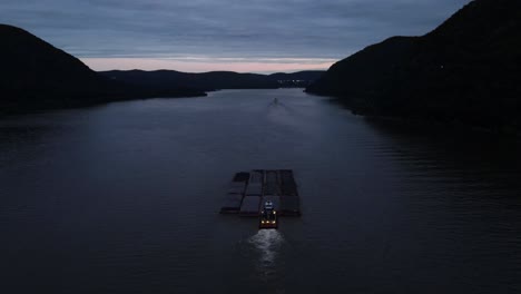 a barge pushing large shipping containers up the hudson river in new york's hudson valley just after sunset