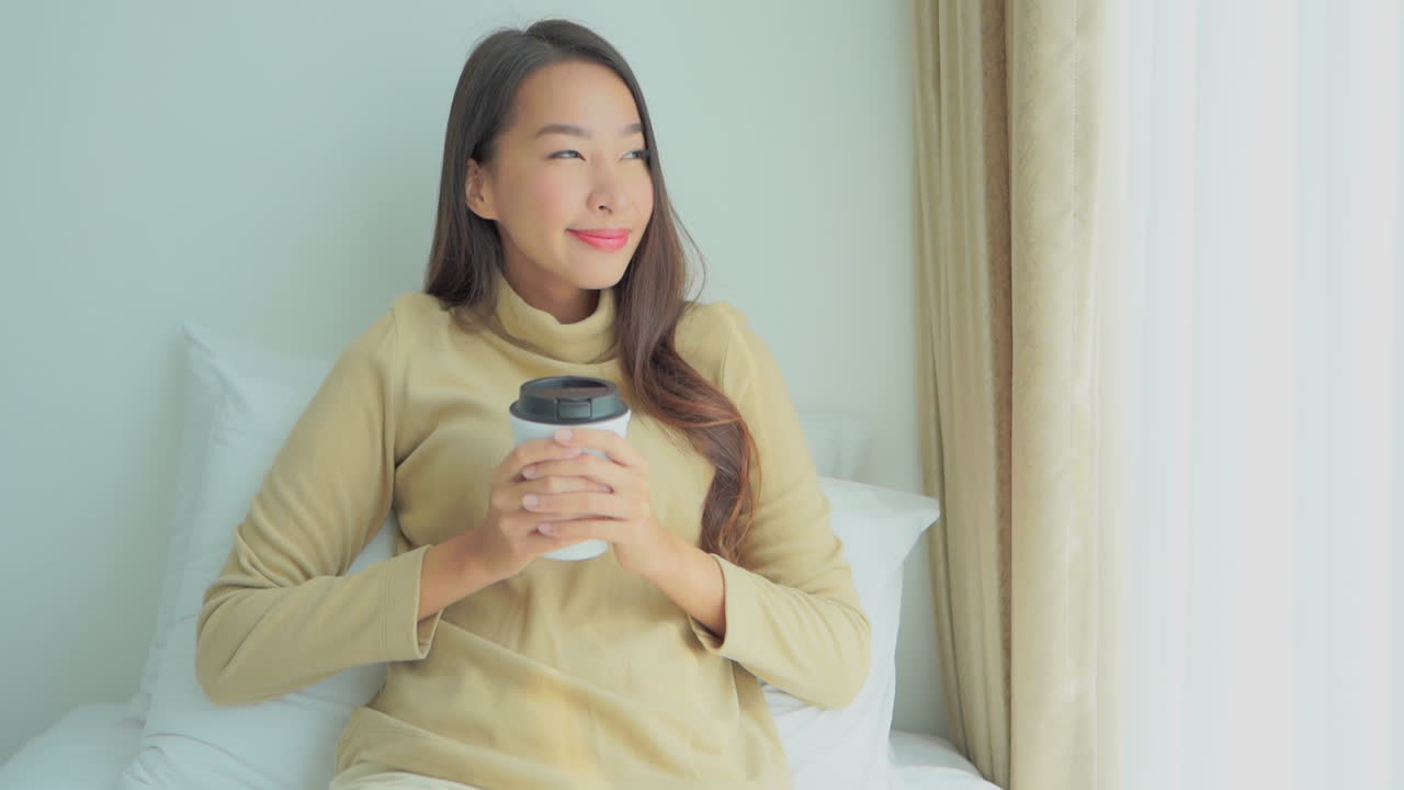 Close -up of a young Asian woman holding a disposable cup of coffee in both hands