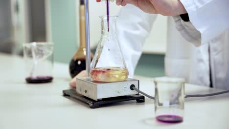 slow motion shot of a scientist mixing different substances in a glass, wearing a white jacket in a lab