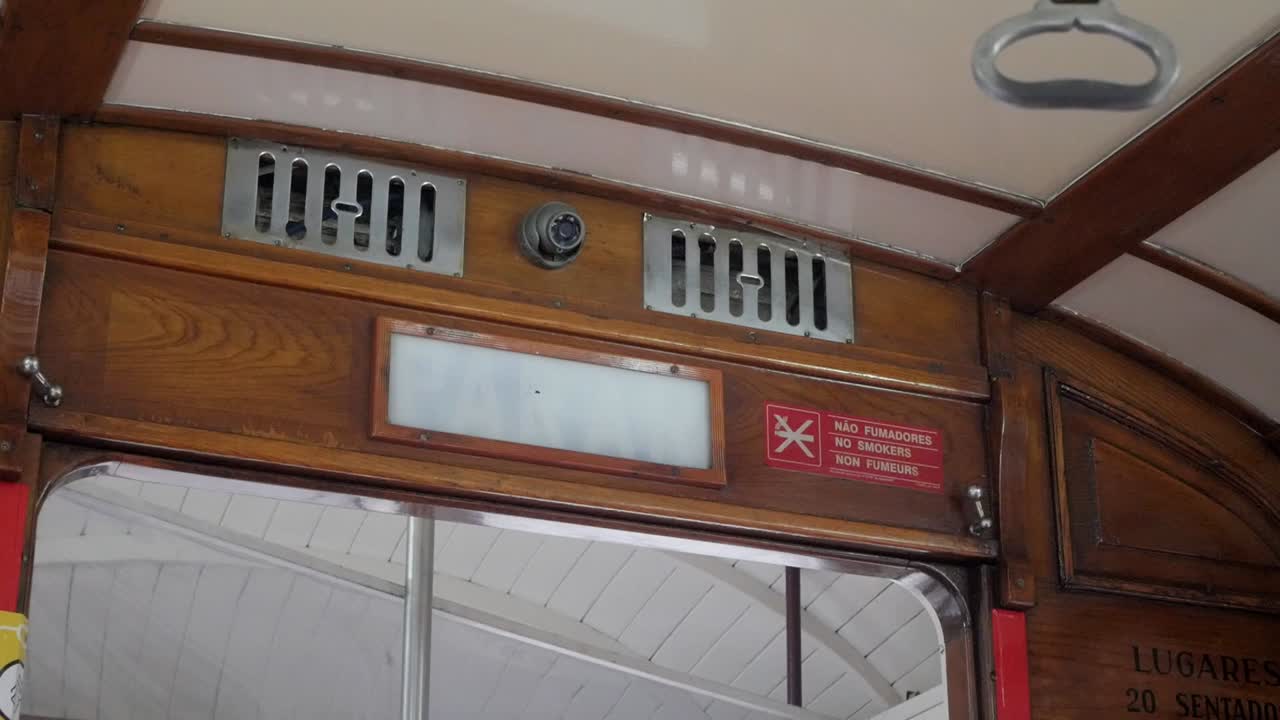 Lisbon historical cable tram next stop announcement sign flashing and safety handle swinging. Vintage transportation vehicle wooden interior. CCTV security camera and ventilation grills above sign.