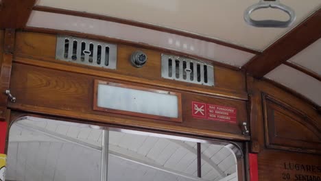 lisbon historical cable tram next stop announcement sign flashing and safety handle swinging. vintage transportation vehicle wooden interior. cctv security camera and ventilation grills above sign.