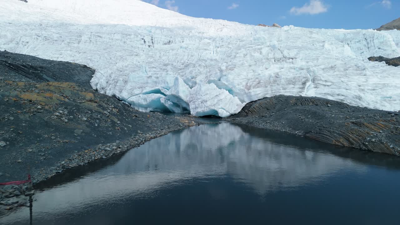 A dramatic aerial drone shot flies towards the terminus of the rapidly melting Pastoruri Glacier, showing the massive ice wall calving into a dark proglacial lake in the Peruvian Andes