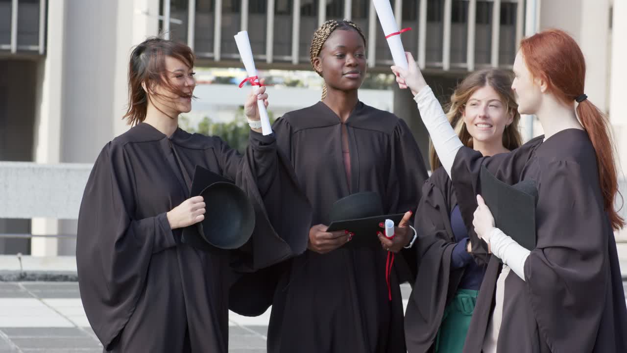 Varias mujeres graduadas caminan por la plaza después de la ceremonia, se ajustan las togas, levantan los diplomas y vitorean