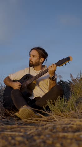 Man playing acoustic guitar outdoors at sunset