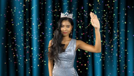 miss beauty pageant asian woman winner stands in front of the stage curtains and waves as confetti falls in celebration of her win