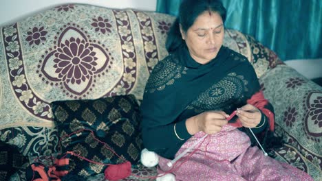 traditional indian woman knitting with red wool and two needle crafts siting in a bed