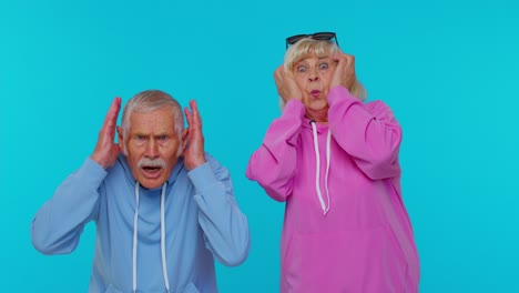 senior couple in hoodies covering their ears in shock