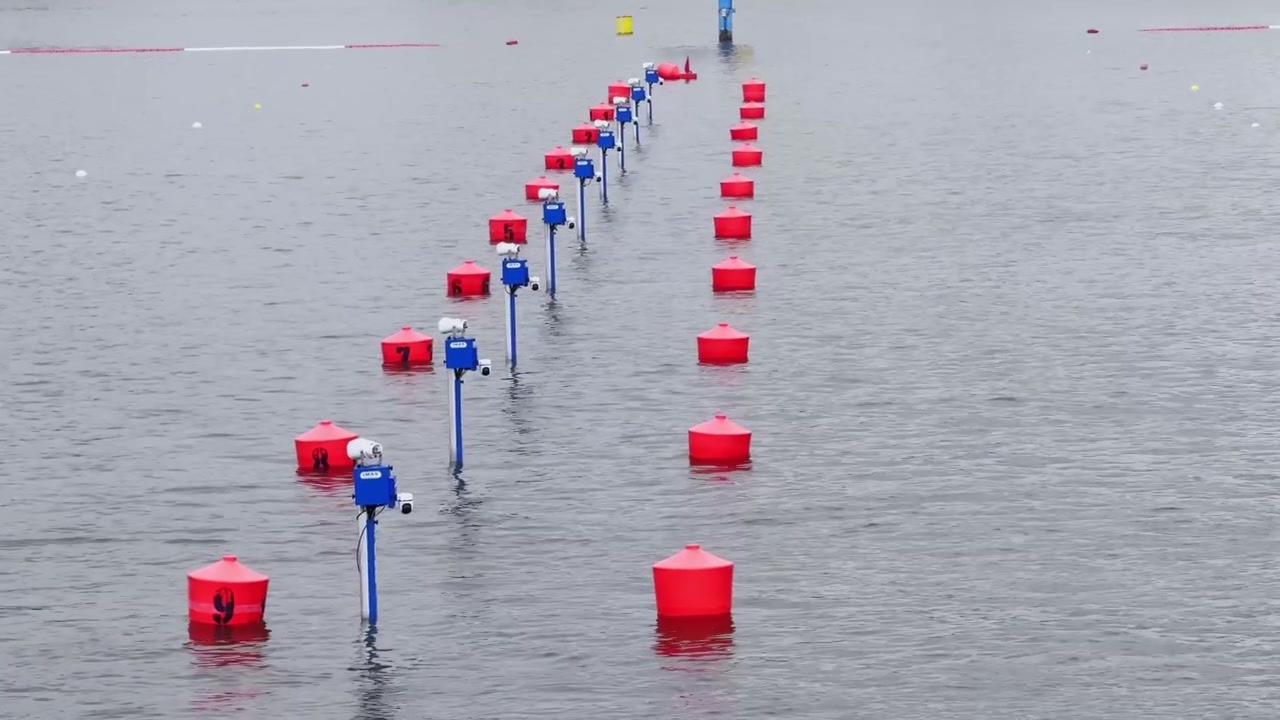 Canoe sprint course markers on a Brandenburg lake, with red lane buoys, blue timing posts, 200 meter sign and calm grey race water.