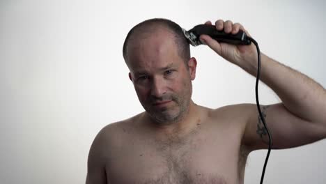 man facing camera while he uses clippers to cut his own hair
