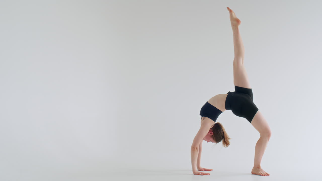Flexible Frau, die einbeinige Rad-Pose in einem weißen Studio ausführt
