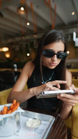 woman using phone while eating fries in a cafe