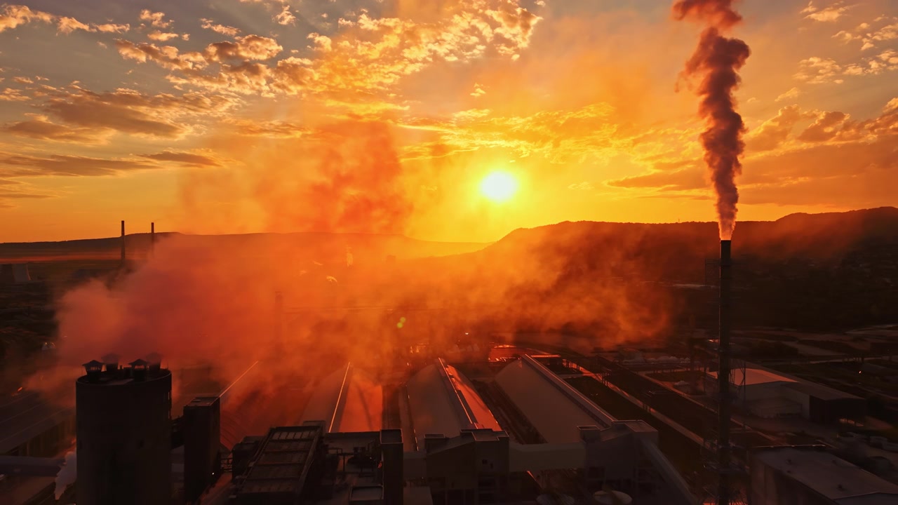 Sunset over industrial area with smoke and bright sky during evening hours