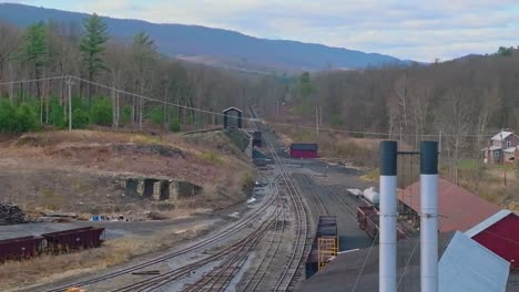 a drone view of an old narrow gauge rail road yard with coal hoppers rusting on a sunny spring day