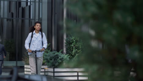 Smiling-businesswoman-riding-electric-scooter-at-downtown-business-center.