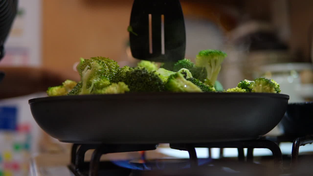 Stirring broccoli on the stove top for a homemade meal - slow motion low angle