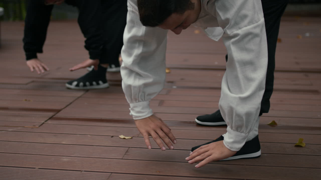 People practicing stretching or martial arts exercises on a wooden deck