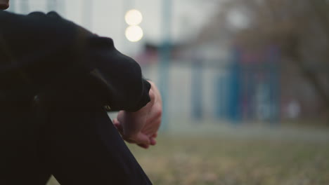 close-up of someone sitting with their hands clasped together, with a blurred background featuring a building and iron poles