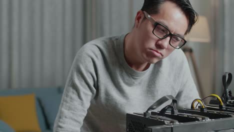 primer plano de un hombre asiático con gafas sacudiendo la cabeza y luego teniendo dolor de cabeza mientras usaba una plataforma de minería para minar criptomonedas