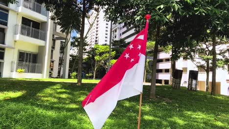 Singapurische-Flagge,-Die-Auf-Dem-Bermuda-gras-In-Toa-Payoh-nachbarschaft-In-Singapur-Steht---Nahaufnahme-Slowmo