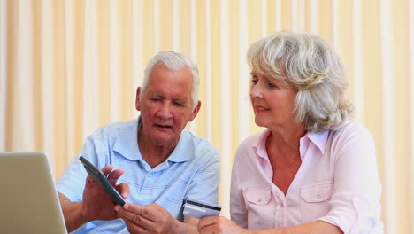 una pareja de ancianos pagando sus cuentas con una computadora portátil.