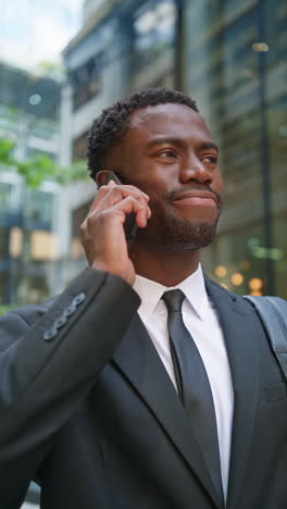 vertical video shot of serious young businessman wearing suit talking on mobile phone standing outside offices in the financial district of the city of london uk shot in real time