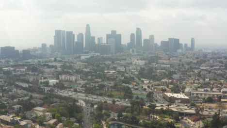AERIAL:-Downtown-Los-Angeles,-California-with-Palm-Trees-and-Highway,-Cloudy,-Traffic