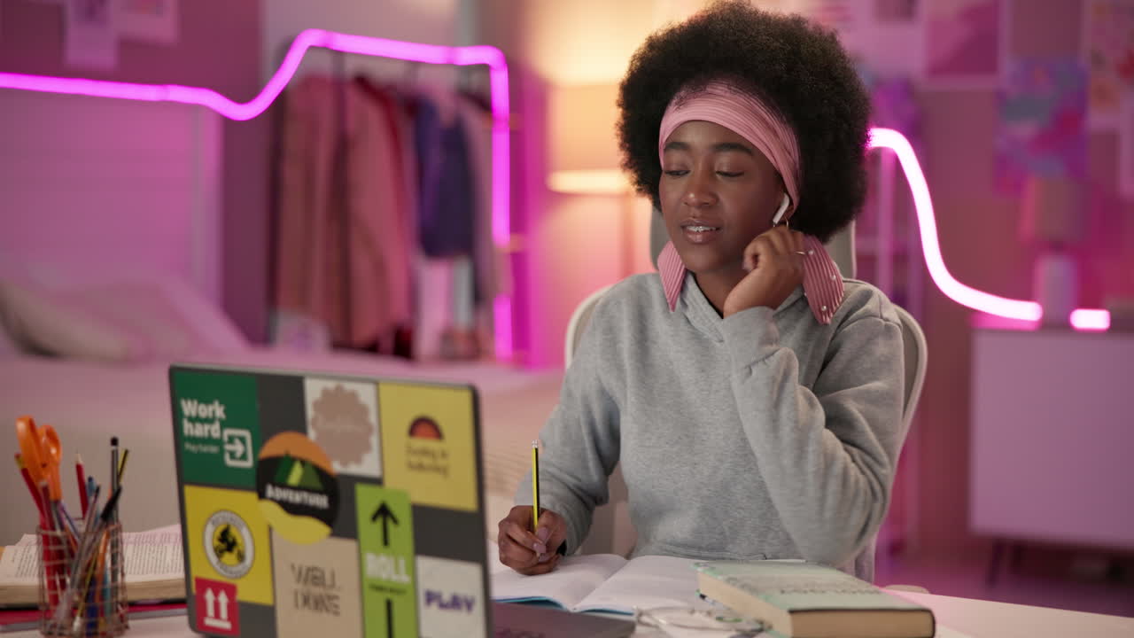 Young woman sitting at her desk in her bedroom, studying and using her laptop.