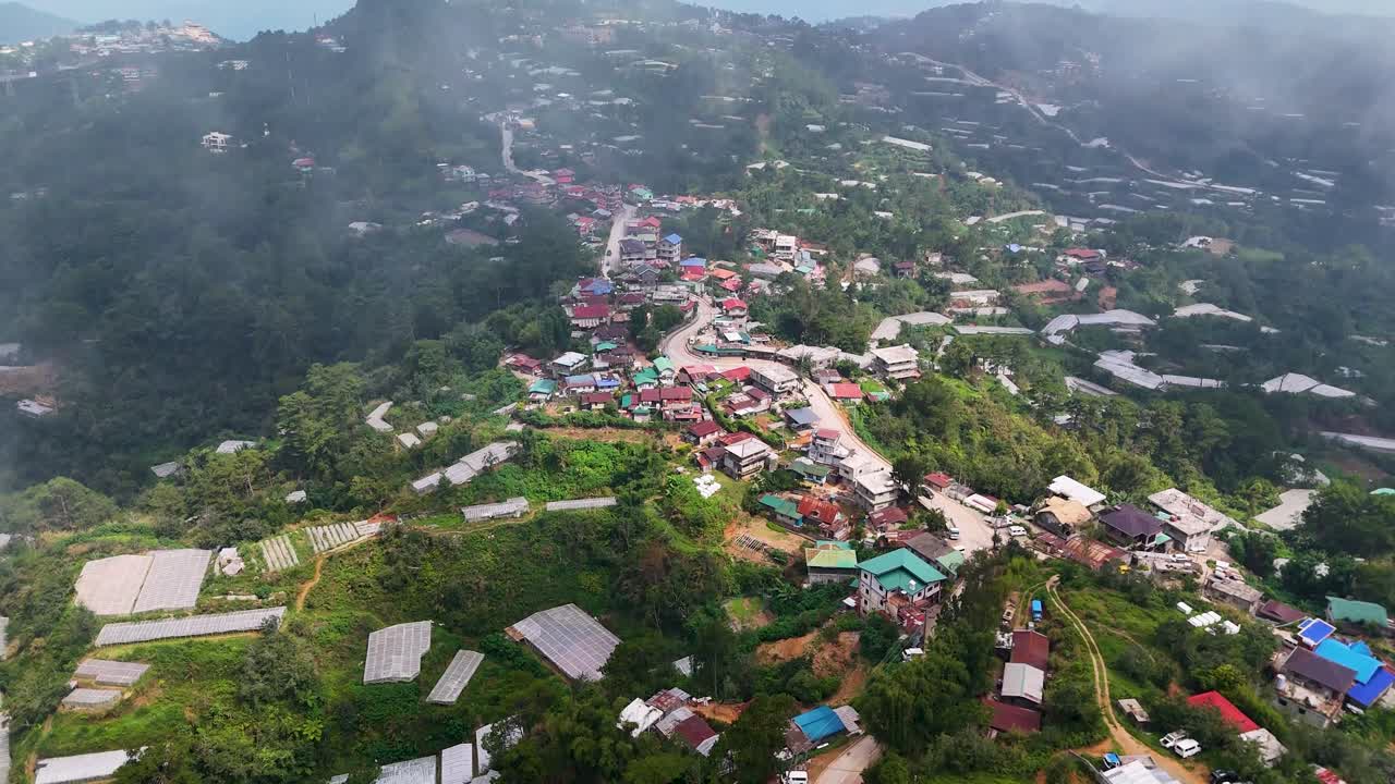 Aerial View of a Misty Mountain Village with Houses and Greenhouses