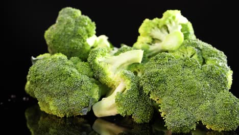 a cluster of broccoli rotates smoothly on a glossy black surface, highlighting its vibrant green color and texture