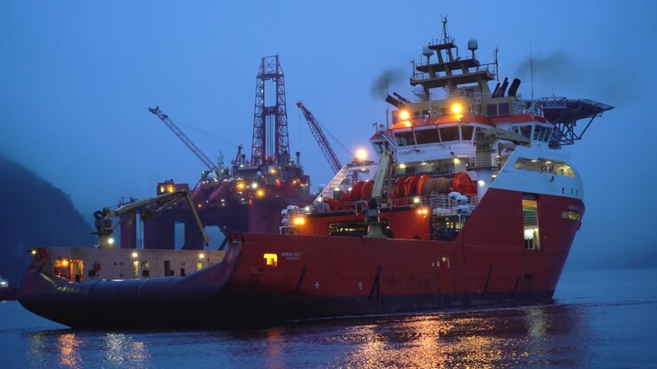 Anchor Handler backing in the Norwegian fjord with an oil platform in the background.