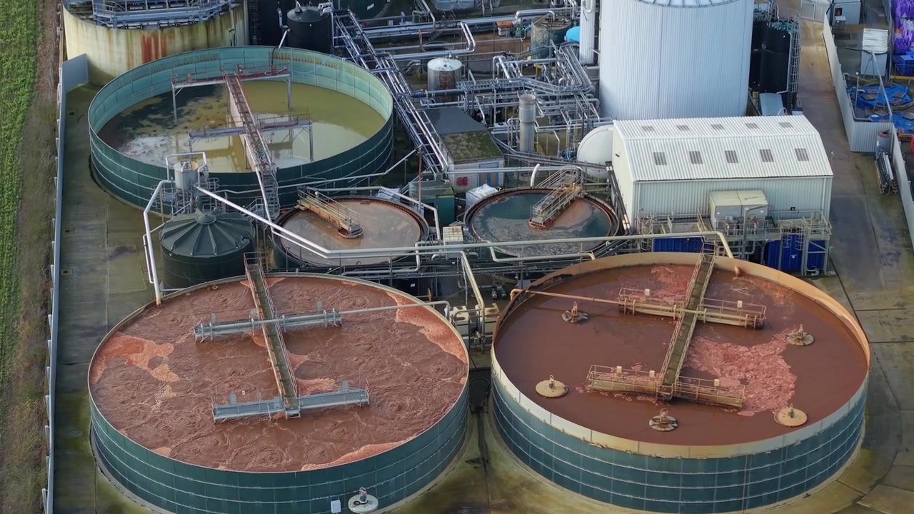 High angle drone view of manufacturing facility cooling towers and silos holding brown processing liquid