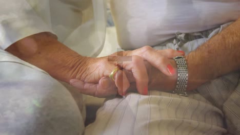 animation of light spots over midsection of senior caucasian couple holding hands