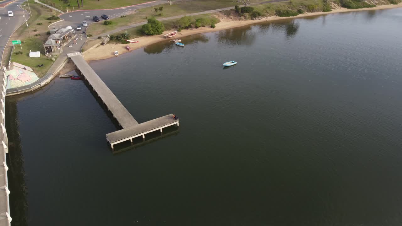 pareja sentada en el borde de la plataforma del muelle del río maldonado junto al puente de forma divertida leonel viera en uruguay