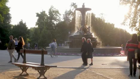 couple walking past a fountain in a sunny park