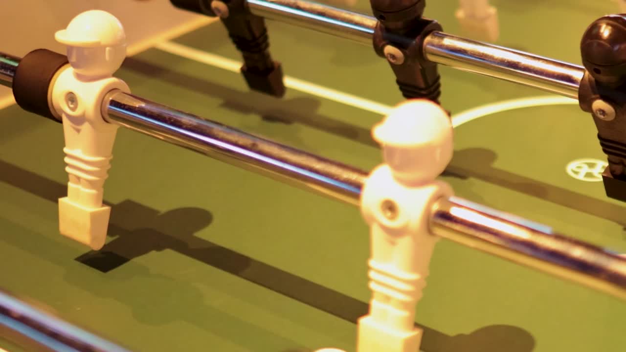 Detailed view of hands maneuvering rods and players on a foosball table.
