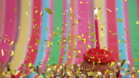 Animation-of-gold-confetti-falling-over-lit-candle-on-birthday-cupcake