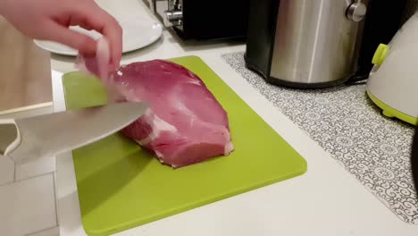 Caucasian-woman-cutting-up-pork-meat-with-a-white-knife-on-a-green-board