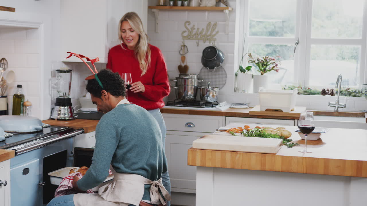 부부가 와인을 마시며 크리스마스 날 저녁을 준비하는 동안 오븐에서 칠면조를 꺼내는 남자