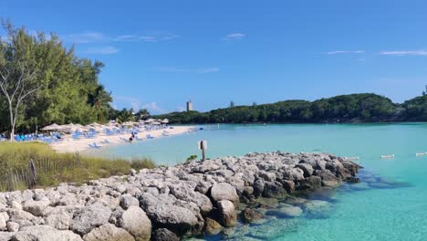 A-paradise-bay-with-rocks-and-a-sandy-beach,-umbrellas-and-sunbeds-in-The-Blue-Lagoon-Island,-The-Bahamas