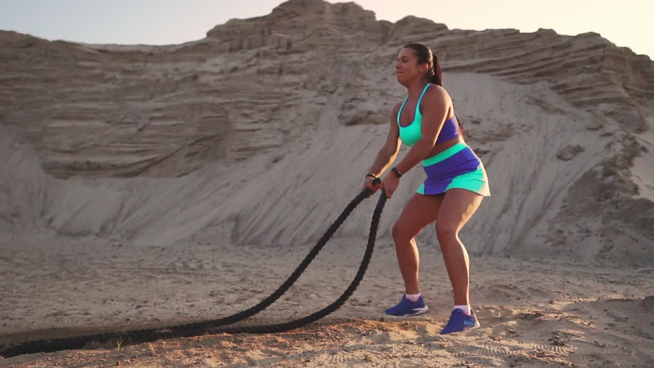 primer plano de una chica con una cuerda realiza entrenamiento al aire libre en el suelo arenoso cerca de la playa. cuerda en las manos de las mujeres al atardecer.