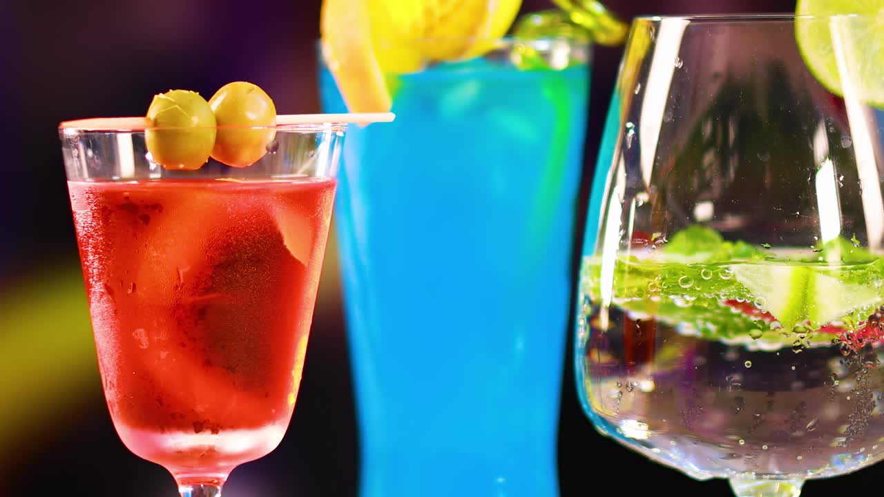 A close-up of three vibrant cocktails with garnishes, set against a dynamic, colorful background.