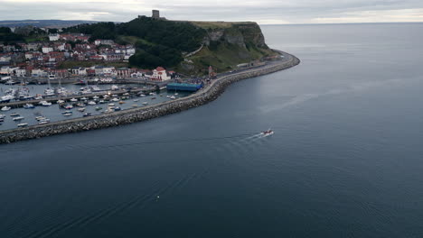 establishing drone shot over scarborough bay and harbour with boat leaving on overcast morning