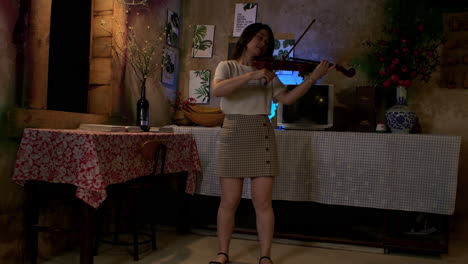 brunette woman playing the violin at home at night